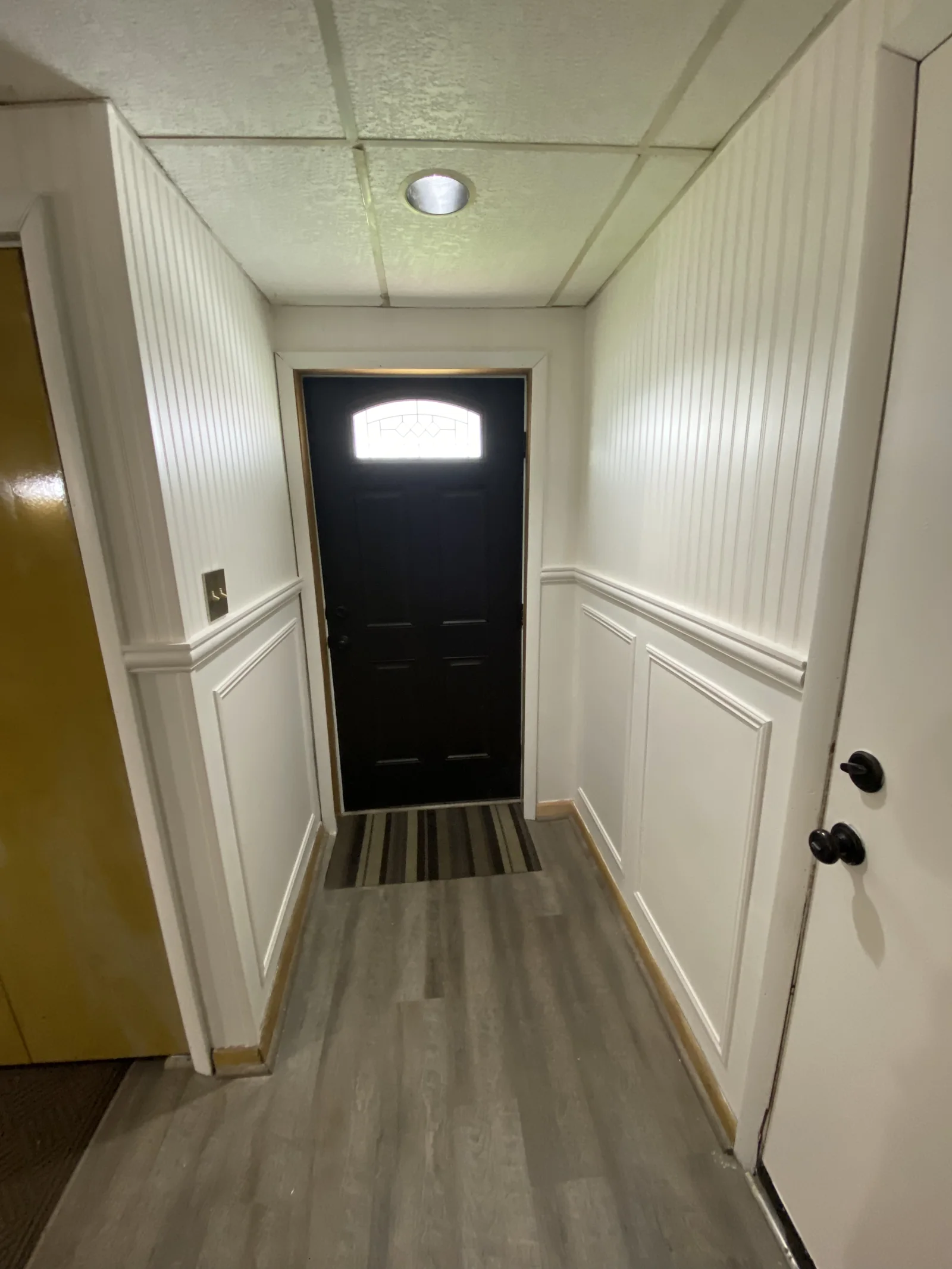Hallway with white beadboard, panel moulding and a dark entry door